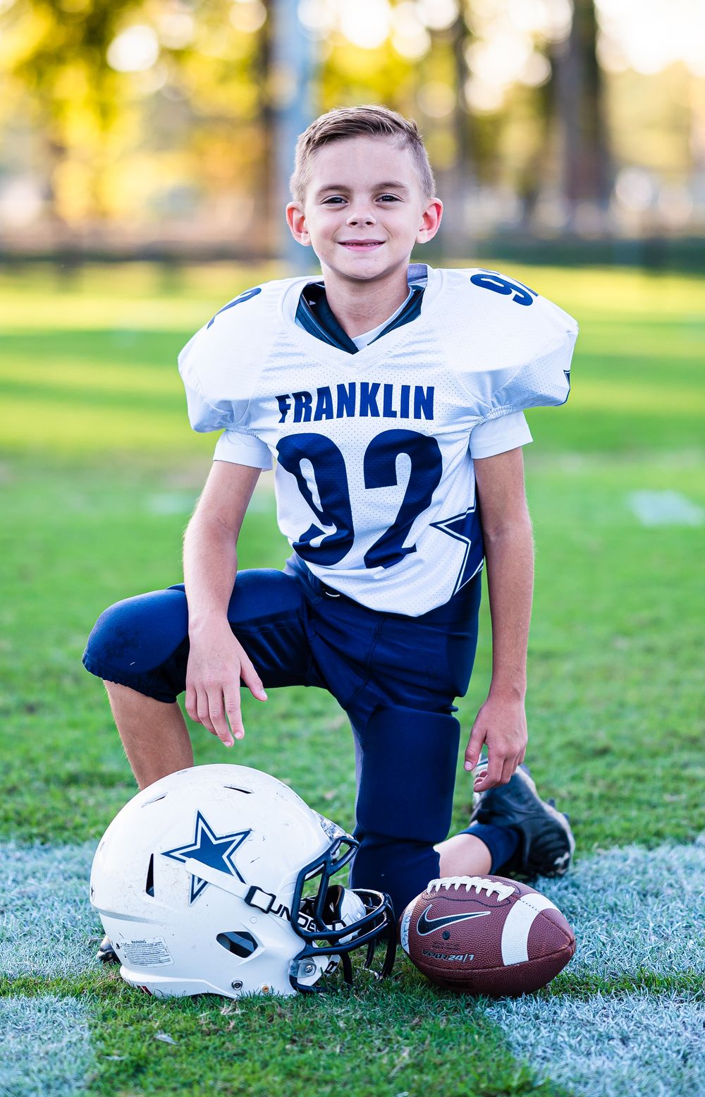 Football equipment including helmets and balls arranged on white sideline of green playing field.