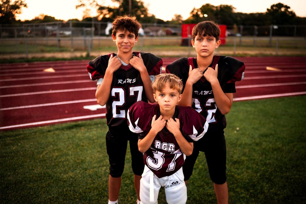 Young football players pose together on a sports field at sunset during practice.
