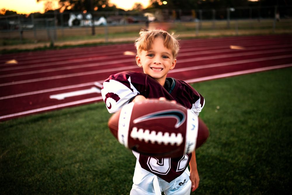 Young athlete in a football jersey poses on a sports field at sunset.