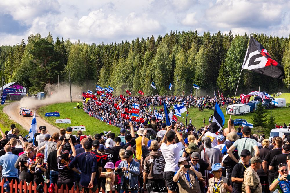 Large crowds of spectators line a mountain bike trail during a downhill racing event in a forested area.