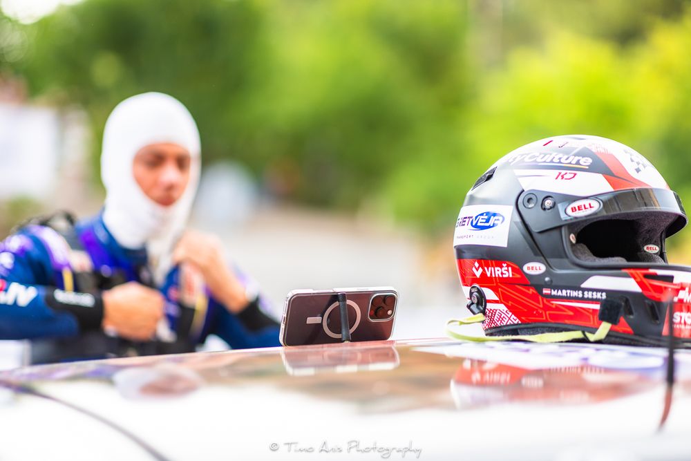 Racing helmet and equipment sit on car hood with blurred background.