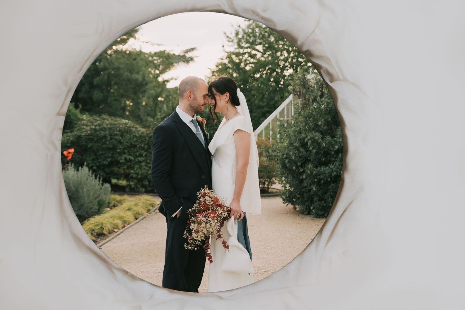 Acrylic wall art orb of a romantic wedding couple embraces in a garden setting during their outdoor photo session.