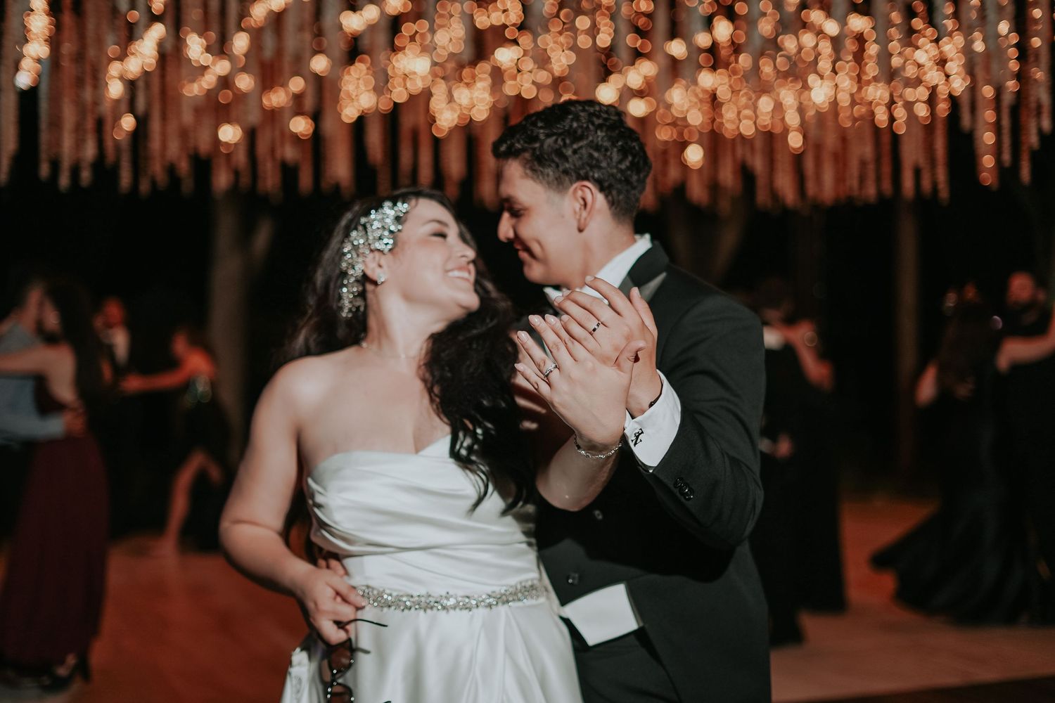 A couple shares a romantic kiss on their wedding day under warm glowing lights during their reception celebration.