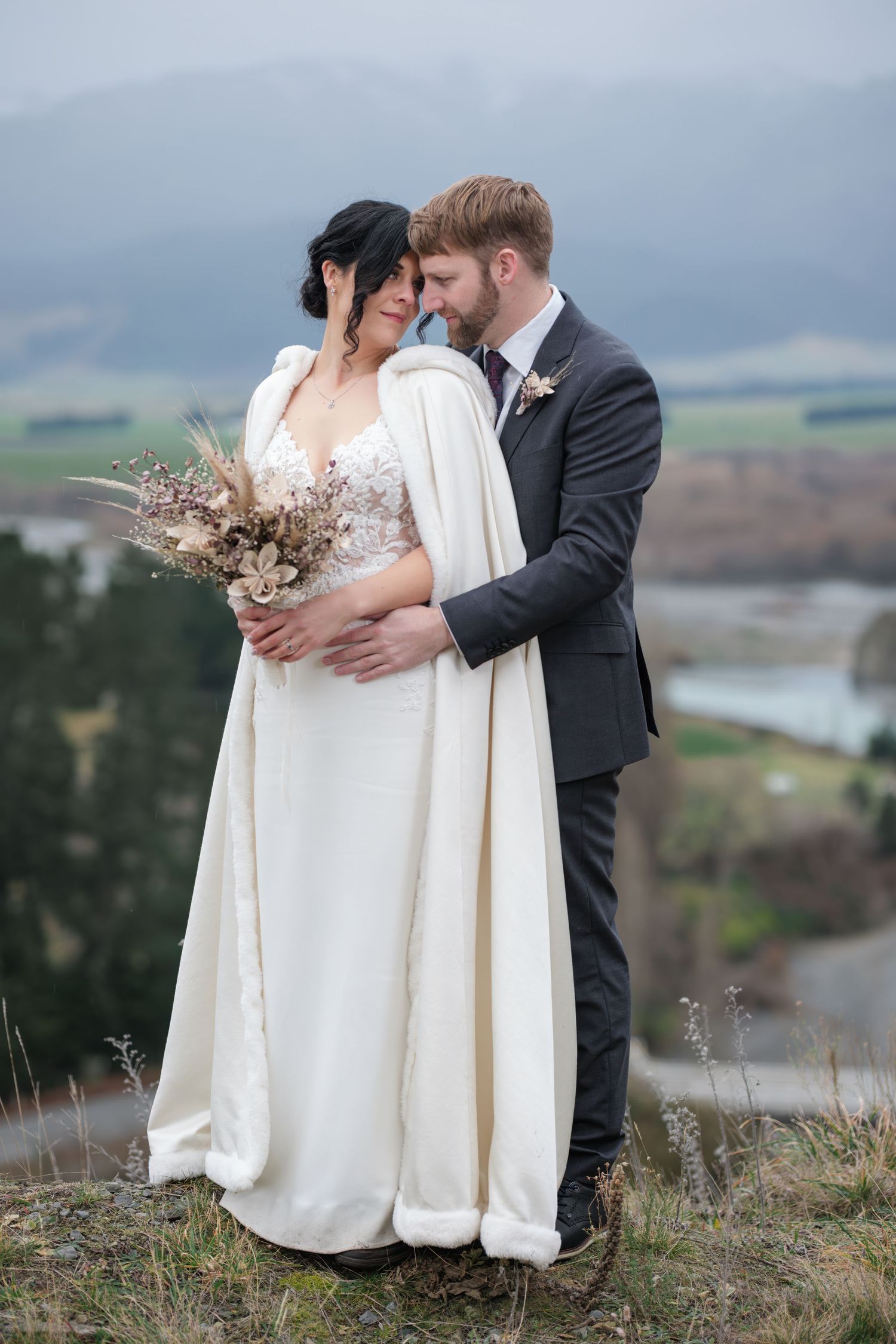 Wedding couple embracing on hilltop overlooking scenic mountain landscape. Hanmer Springs