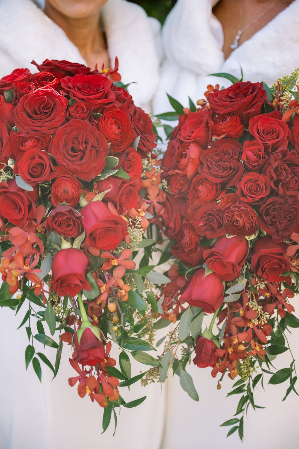Close-up of stunning red rose bouquets with green foliage against white dresses.