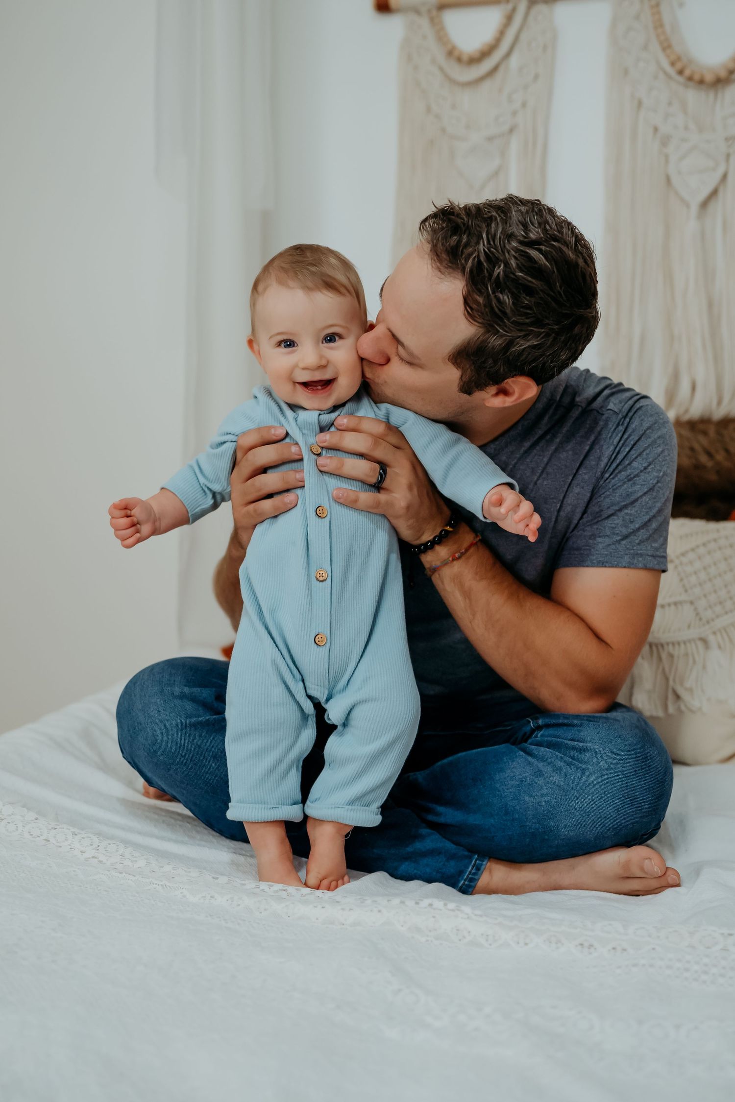A tender moment between parent and baby in light blue romper on white bedding in a series of four connected photos.