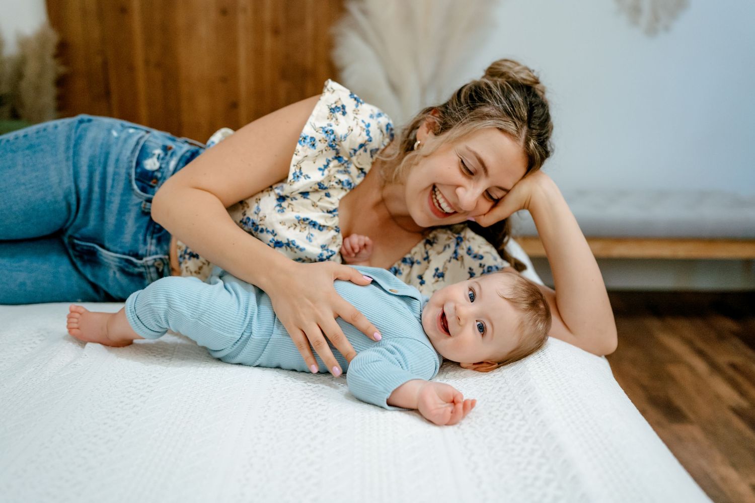 Parent and child playing together on a white bed in a cozy bedroom with wooden floors.