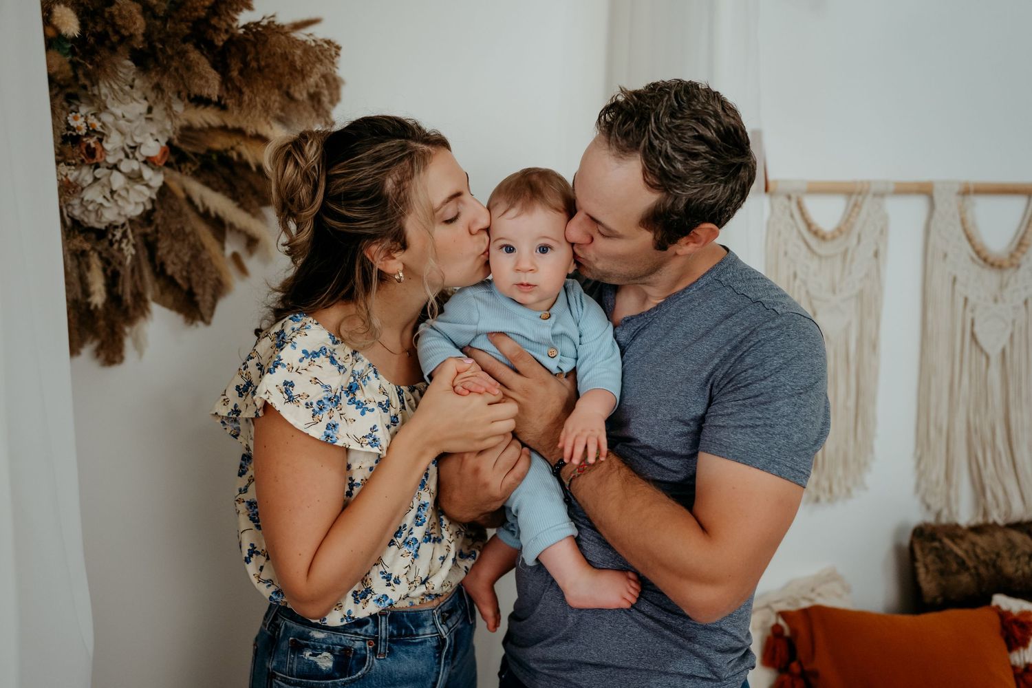 A family shares a tender moment together in front of a wall decorated with dried flowers and macrame.