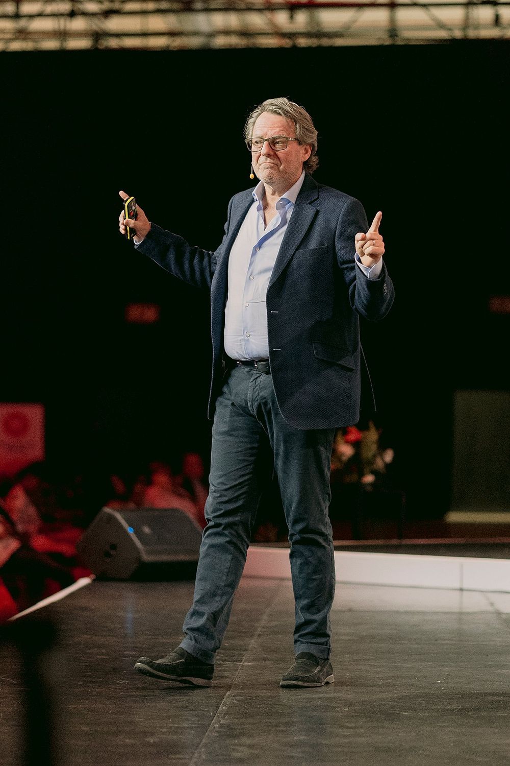 Dynamic male speaker gesturing on stage holding phone during conference presentation.