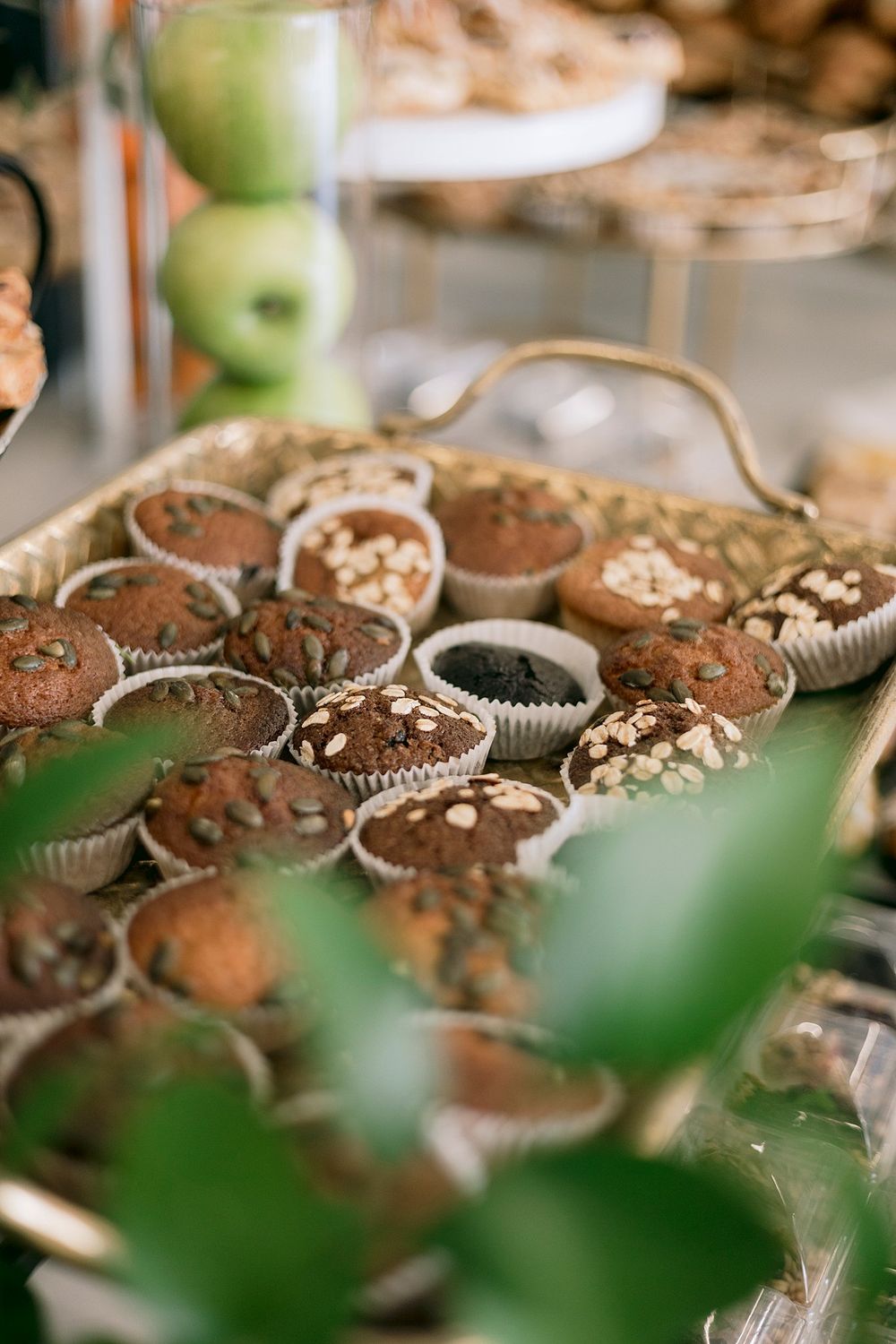 Assorted chocolate muffins topped with oats and seeds arranged on a gold serving tray at a catering display.