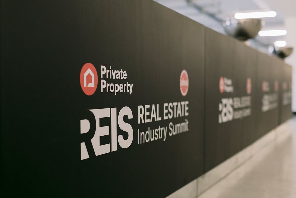 REIS Real Estate Industry Summit branded black exhibition wall with Private Property logos repeated in sequence.