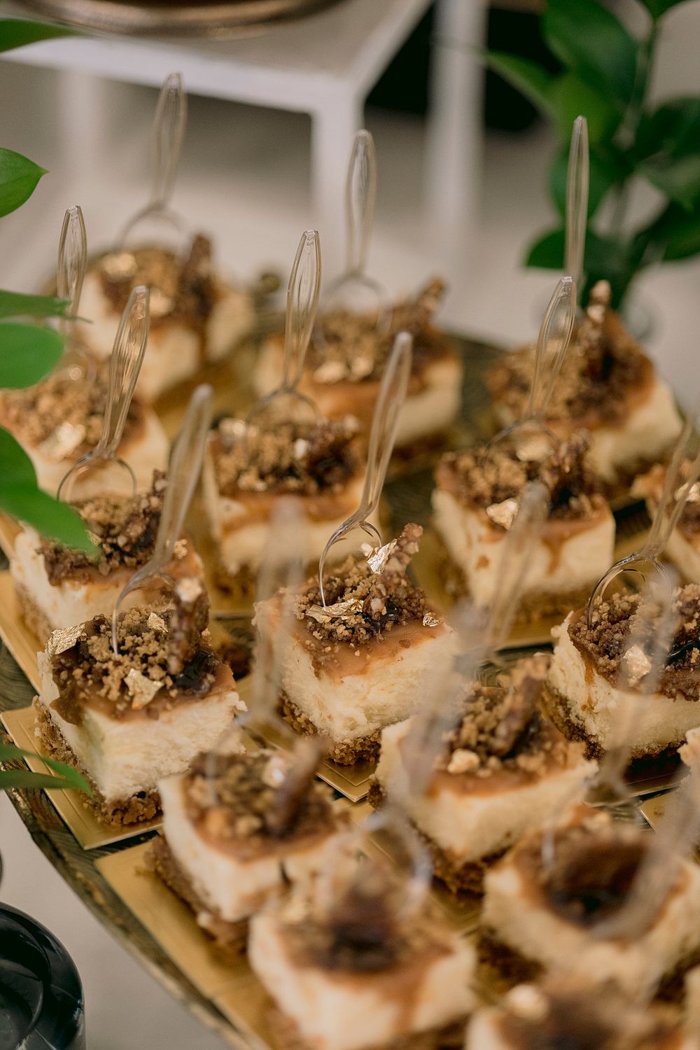 Elegant bite-sized cheesecake desserts with nut topping served on gold tray with mini forks.
