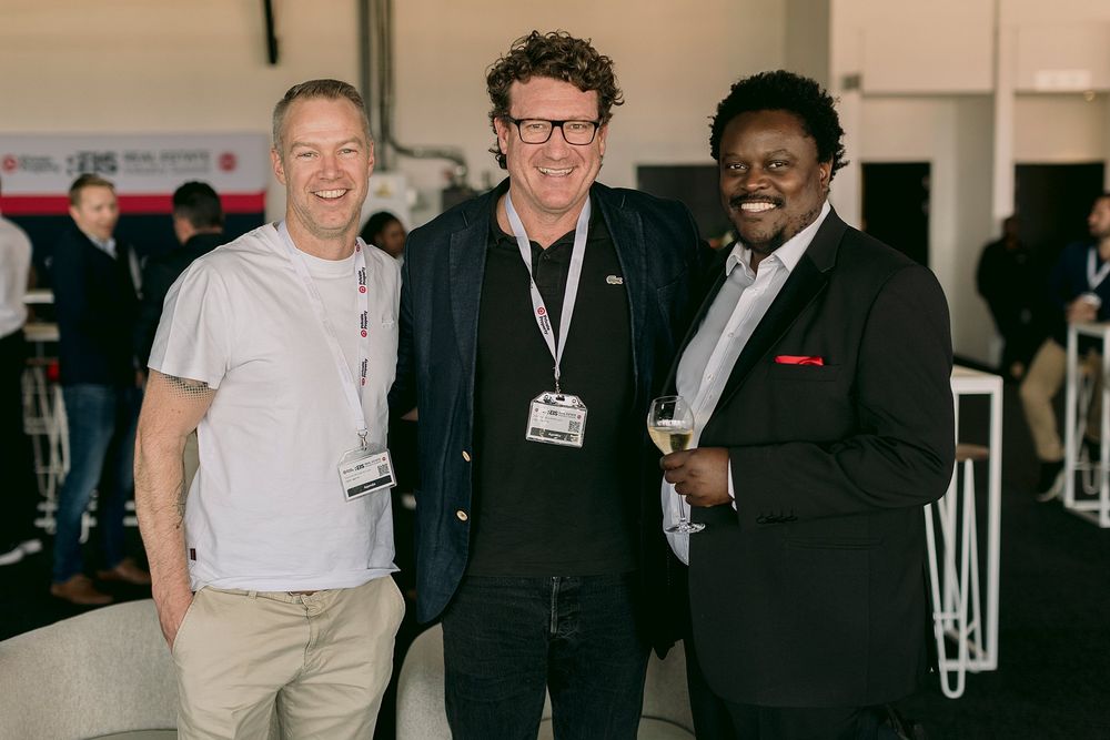 Three men smiling and posing together at a professional real estate networking event.