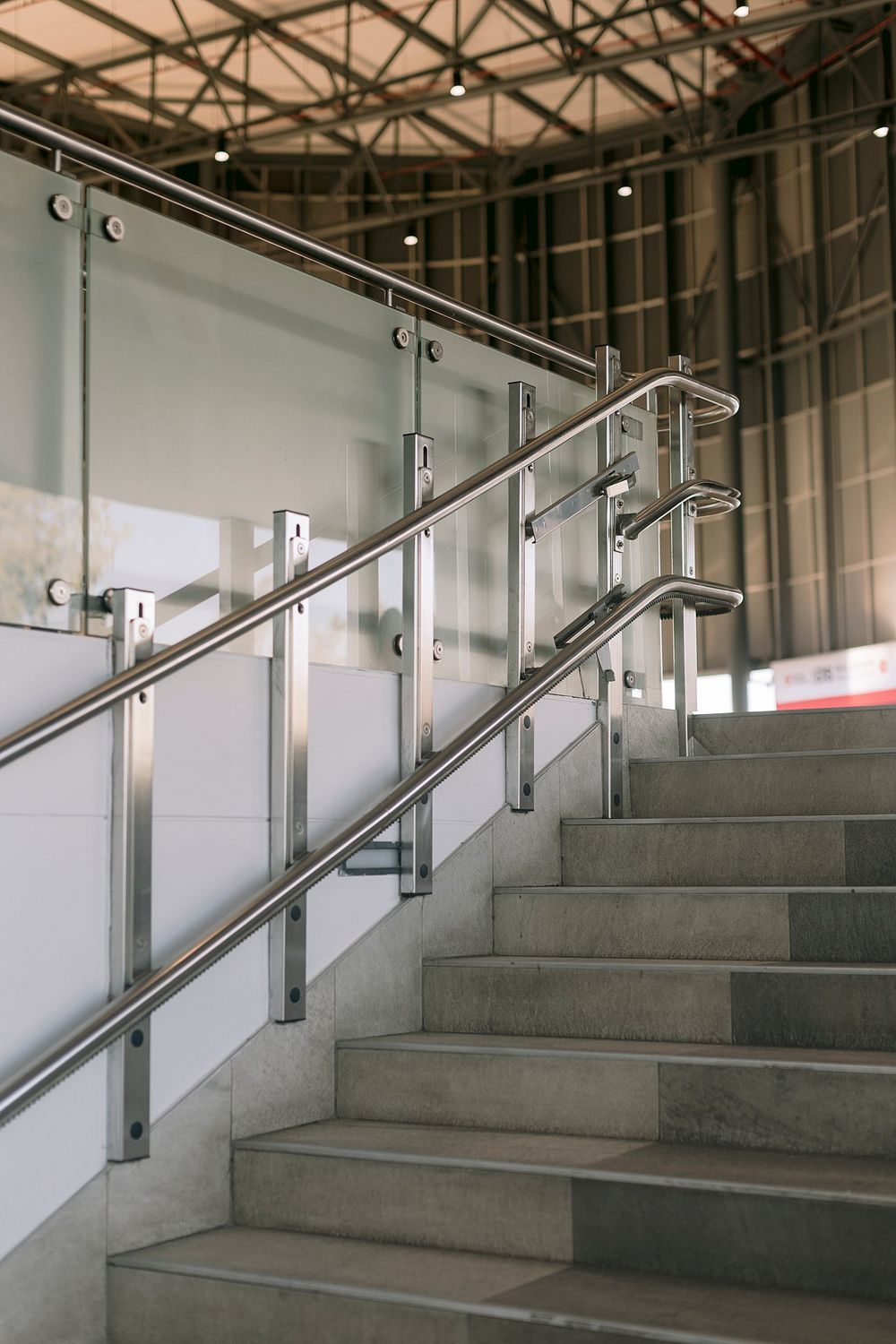Modern concrete staircase with stainless steel handrails and glass panels inside an industrial venue.