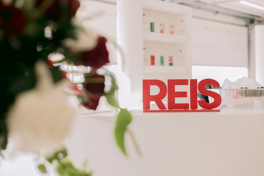 Red REIS logo letters displayed on a white reception desk decorated with red and white flowers.