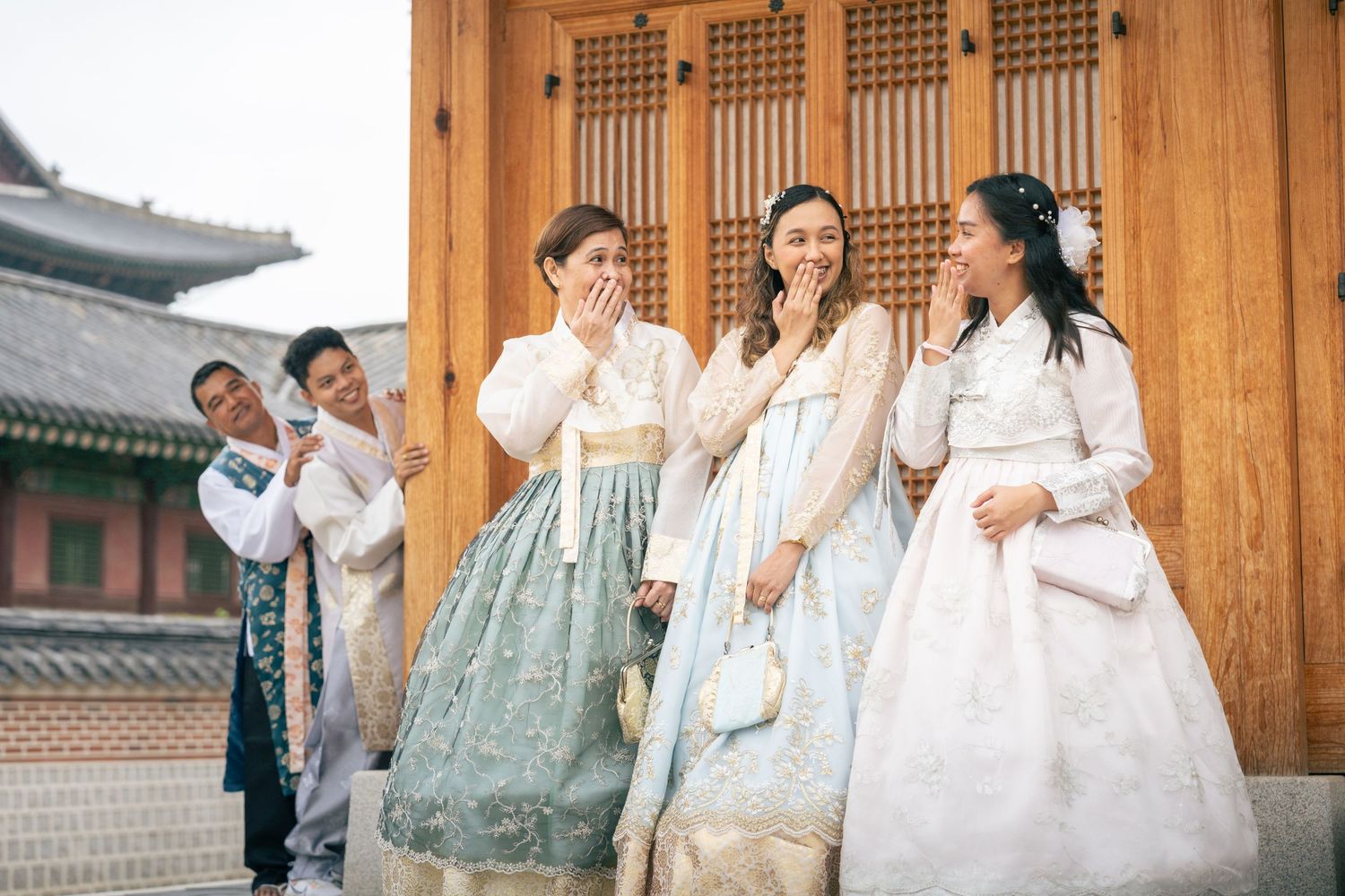 A group wearing traditional Korean hanbok clothing poses together outside a traditional wooden temple building.