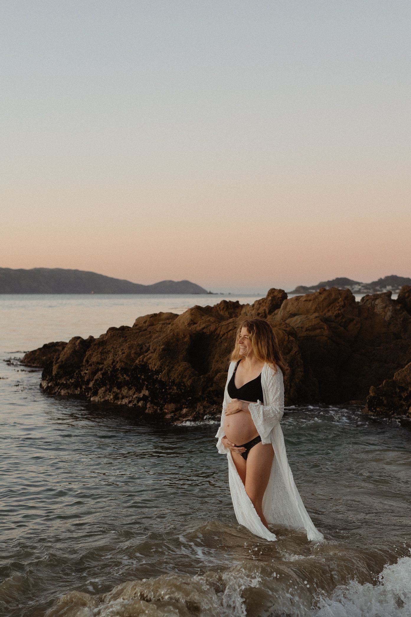 A romantic sunset photoshoot on rocky coastal cliffs with mountains and ocean views at golden hour.