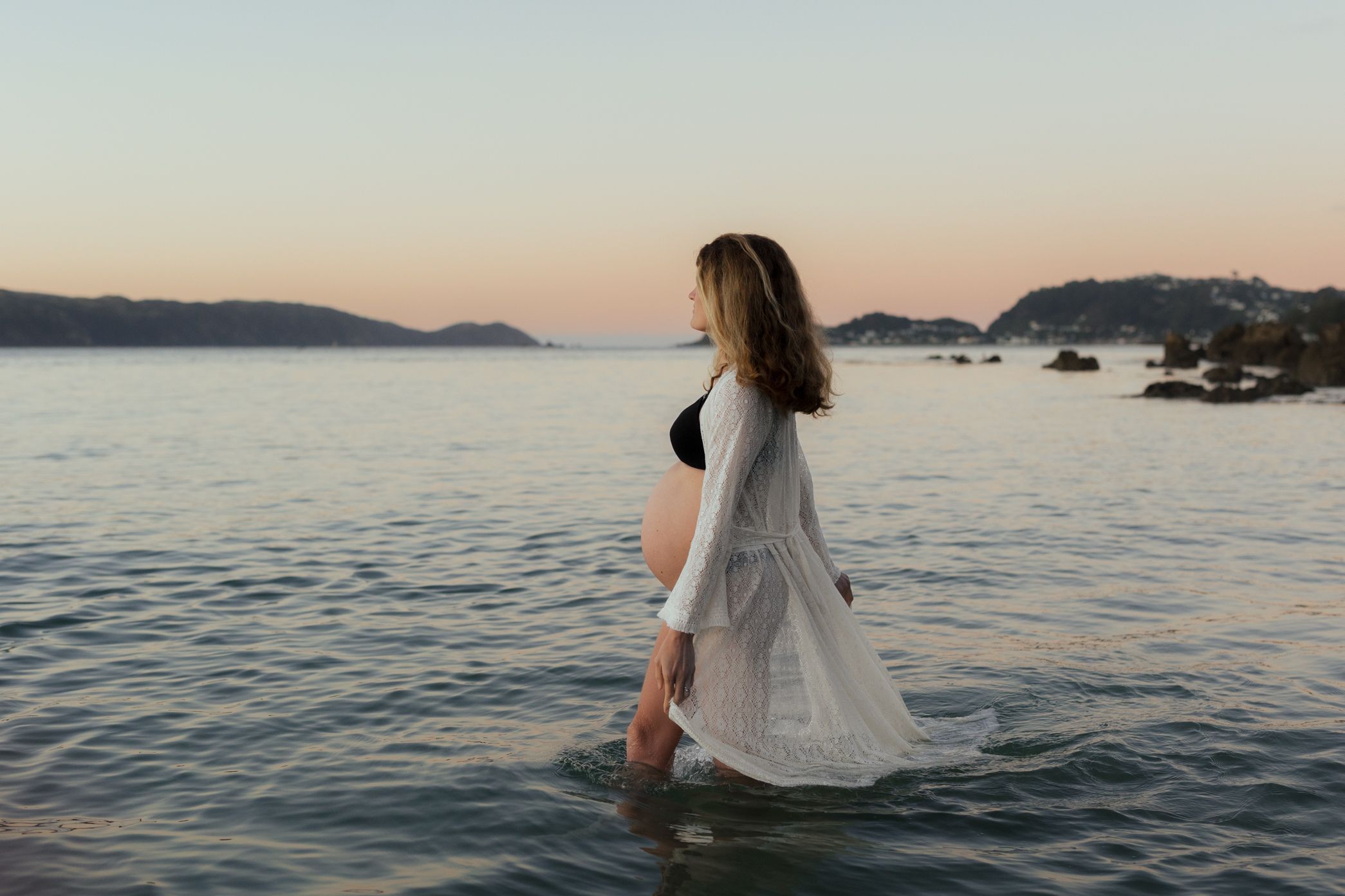 Scenic coastal wedding photoshoot at sunset with mountains and calm ocean waters in the background.