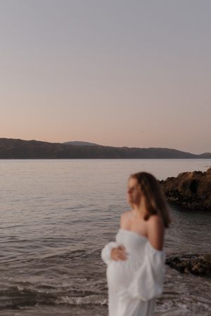 A serene coastal scene at sunset with silhouettes against the ocean and rocky shoreline.
