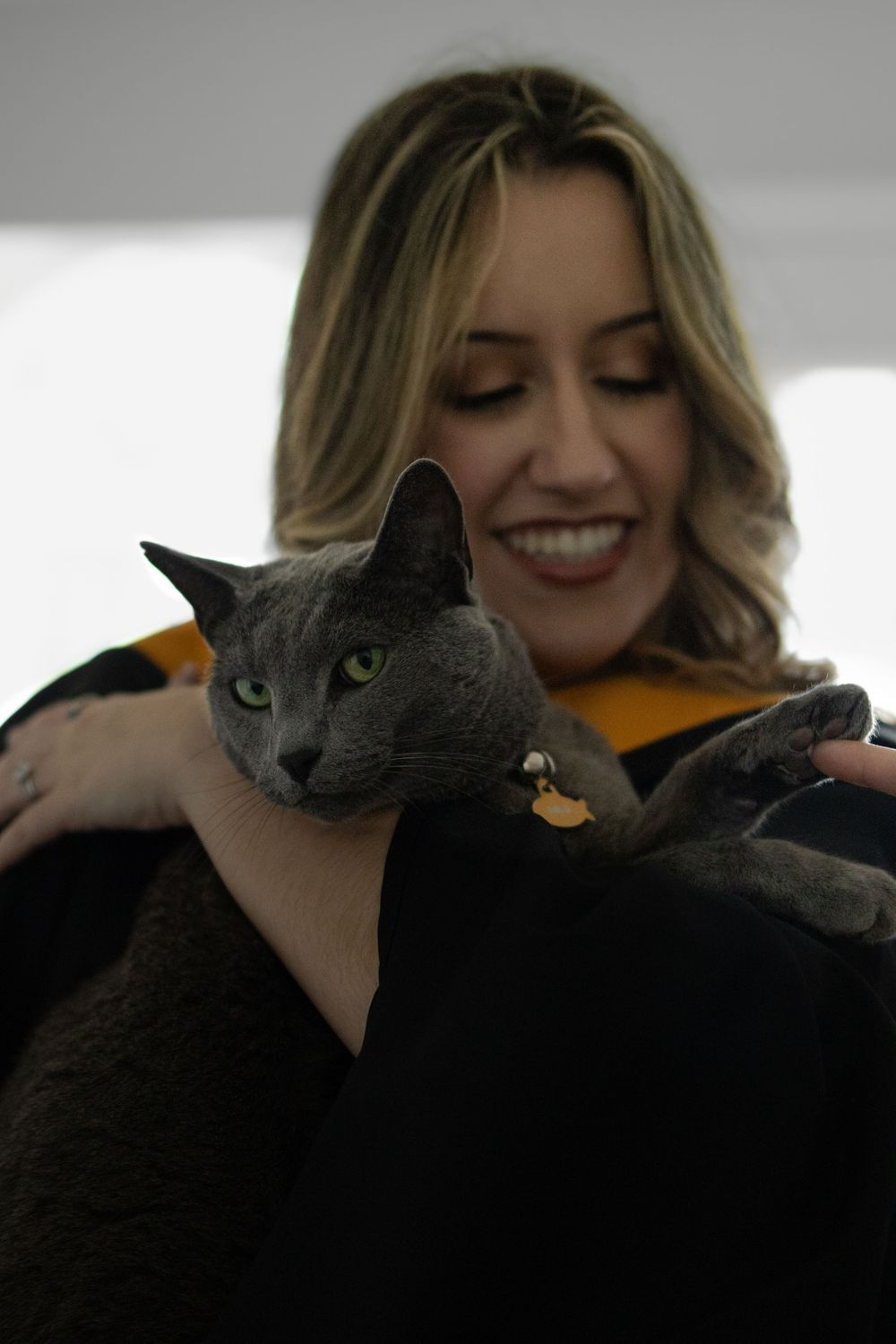 A grey cat with bright eyes being held and cuddled by someone wearing a yellow sweater.