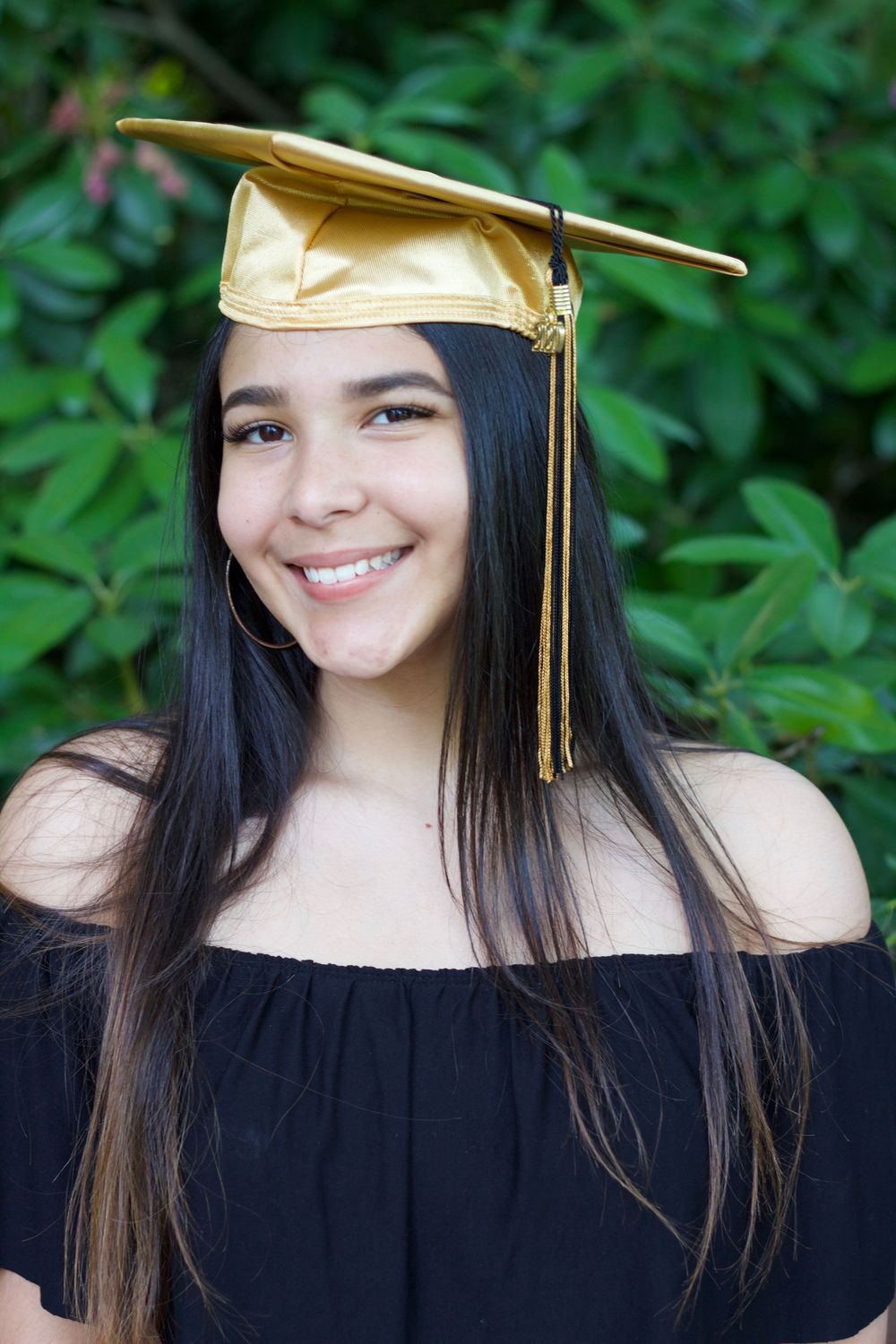 Graduation portrait series showing a graduate in black off-shoulder top and gold cap against green foliage background.