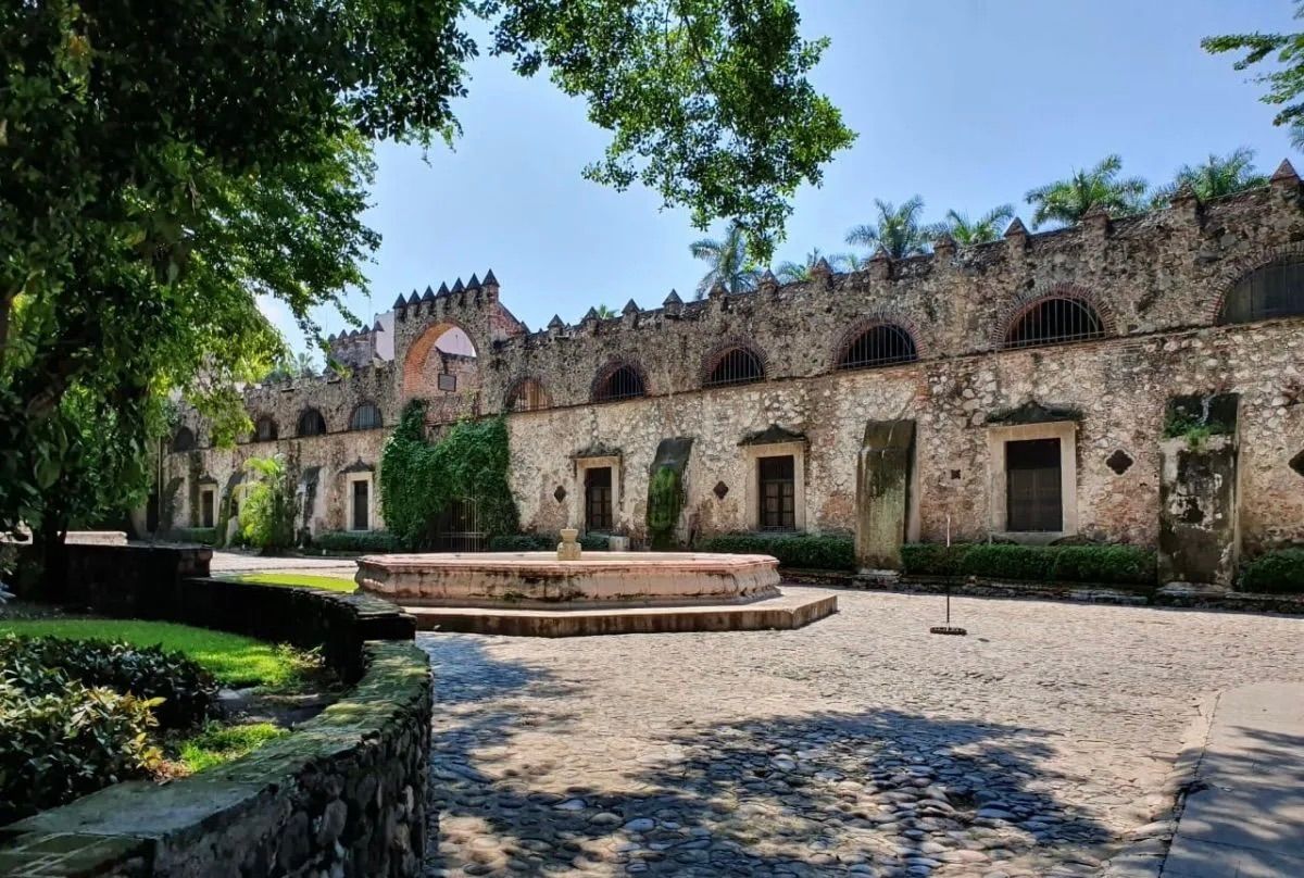Ancient stone courtyard with arched walkways and lush greenery in a historic Mexican hacienda setting.