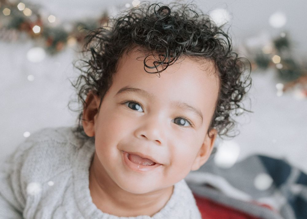 A young child with curly hair smiles joyfully in a series of candid holiday photos.