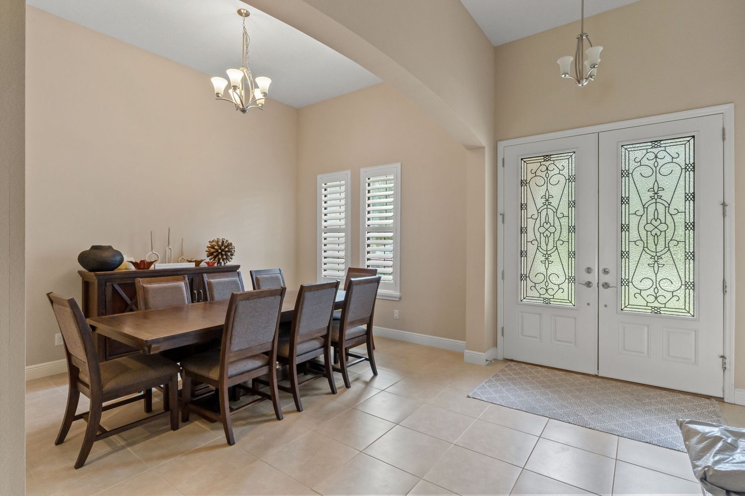Spacious dining room with tile floors, chandelier, and large windows letting in natural light.