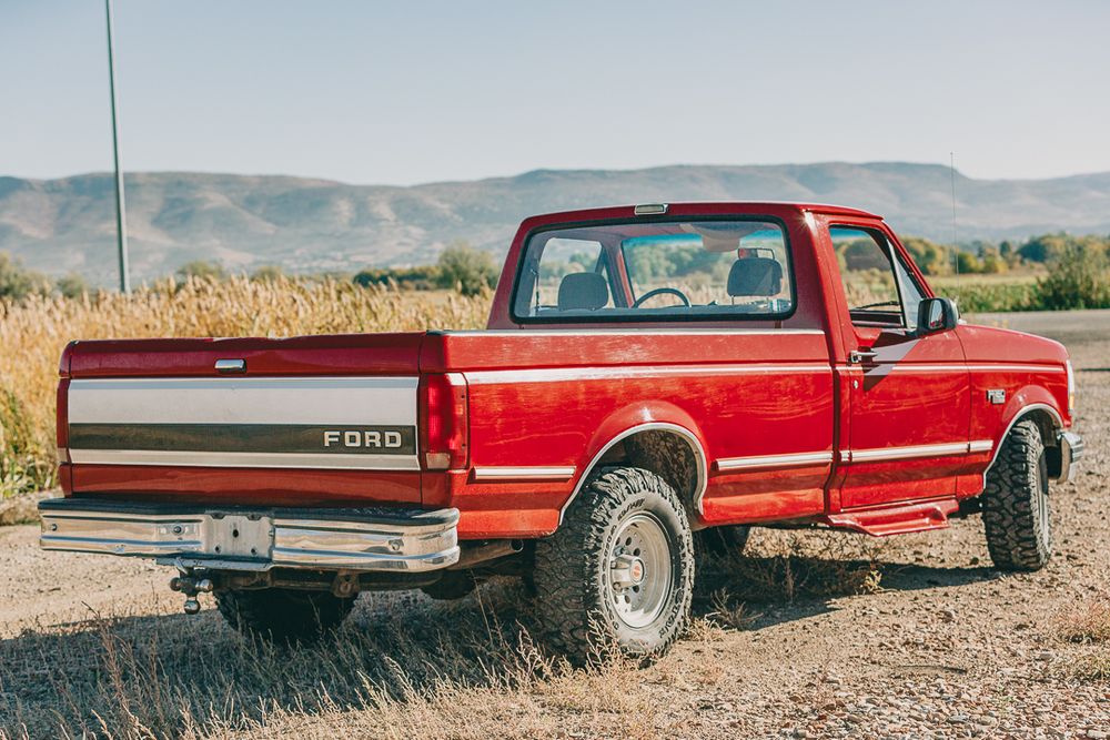 Red Ford pickup truck parked on gravel with mountains in the background.