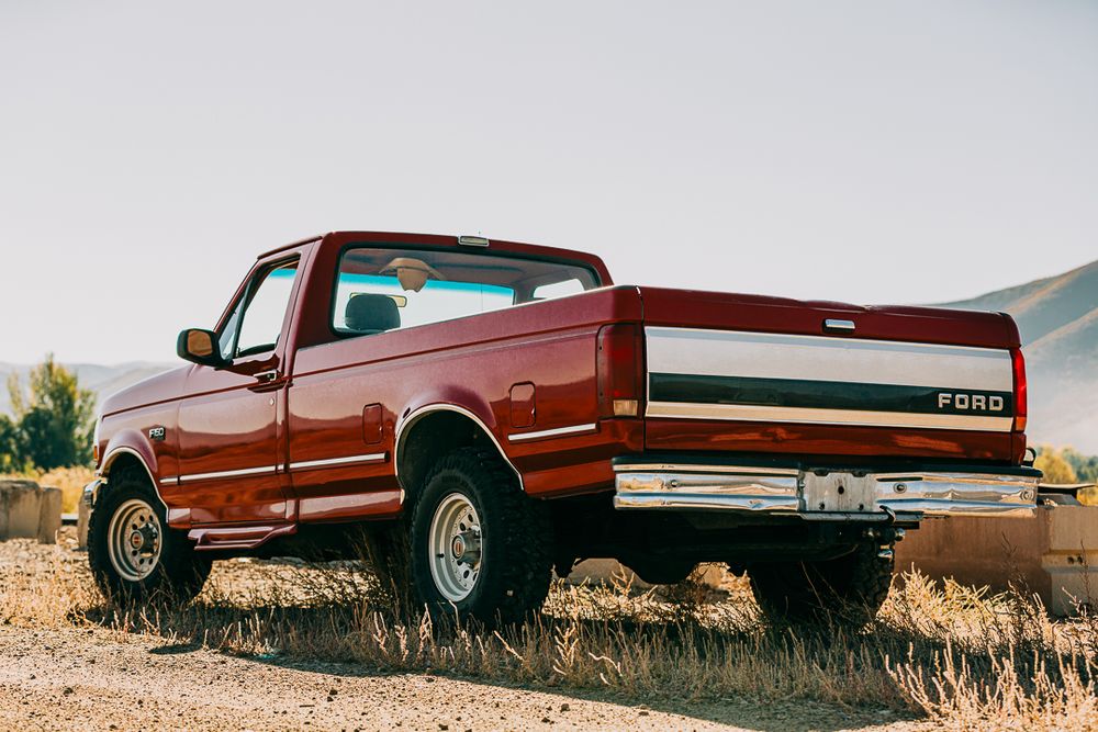 A vintage red Chevrolet pickup truck parked on a hill with mountains in the background during golden hour.