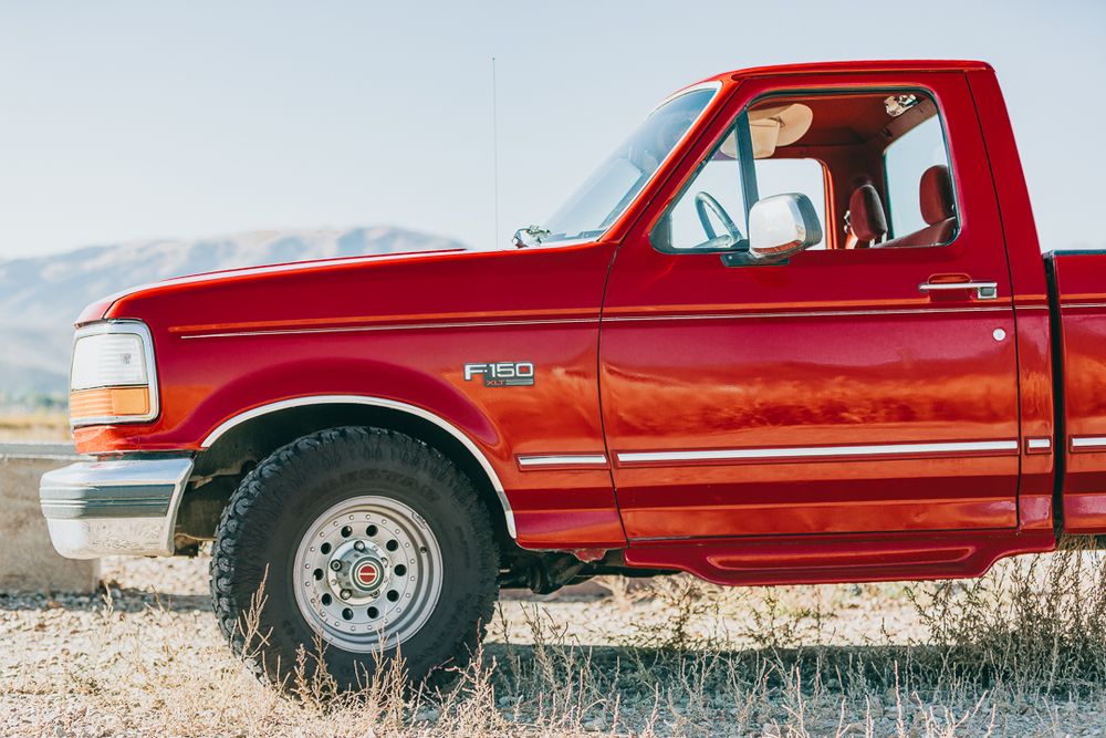 A vintage red Ford F-150 pickup truck parked in a desert landscape during golden hour.