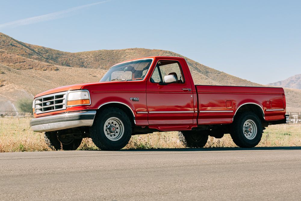 Red pickup truck parked in desert landscape with mountains in background.