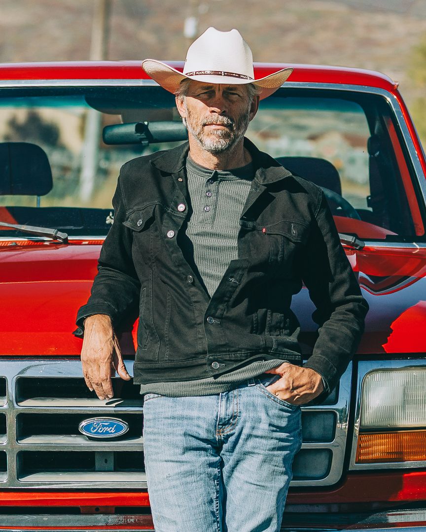 A red Ford pickup truck parked with someone in western attire leaning against the door in a rural setting.