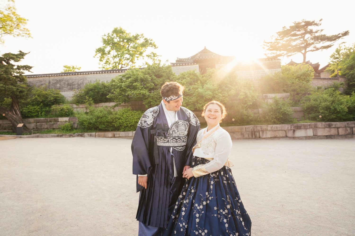 A couple shares a tender moment in a garden at sunset while wearing formal attire.
