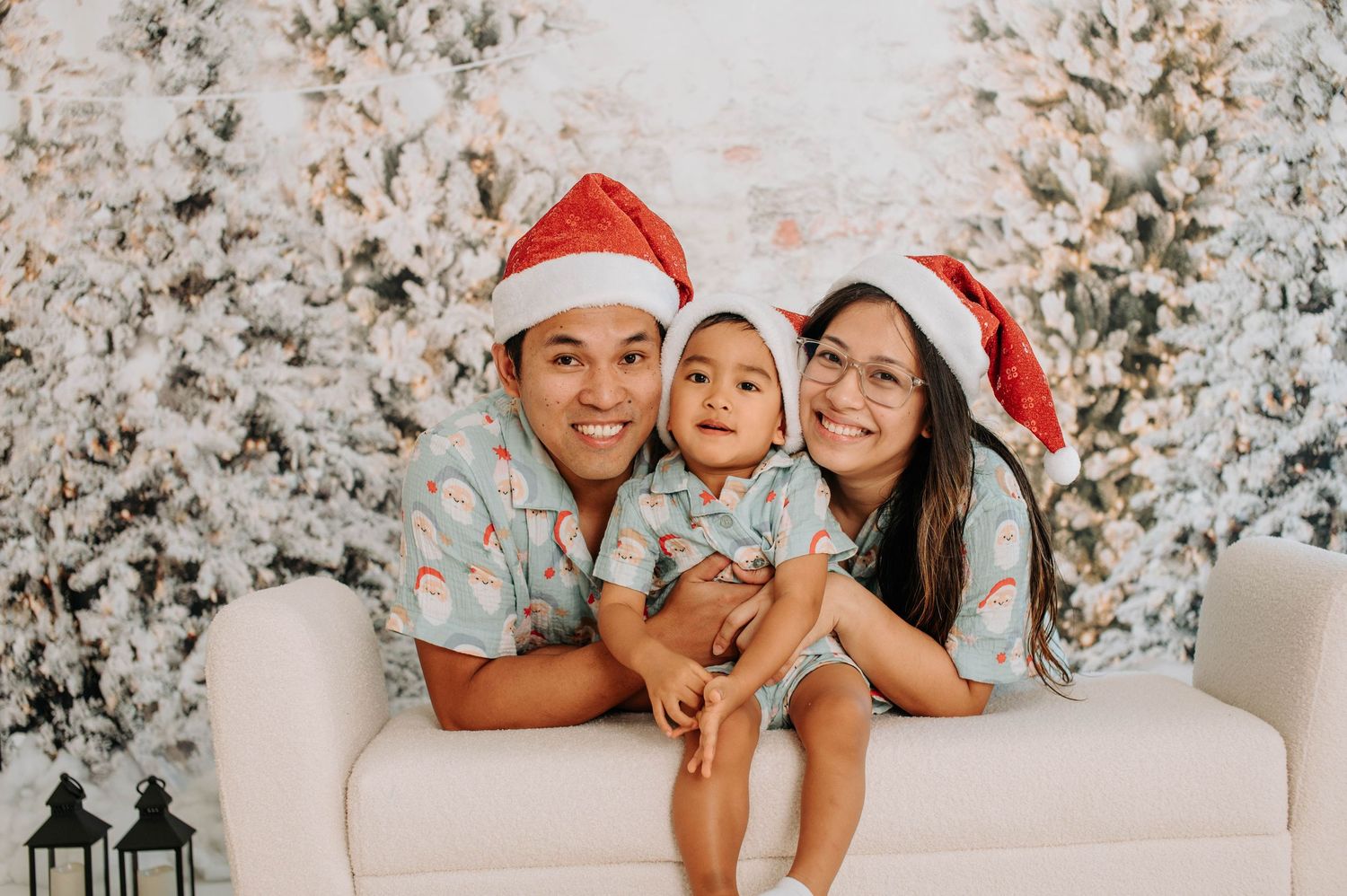 A family wearing Santa hats poses together on a white couch with snowy winter decorations in the background.