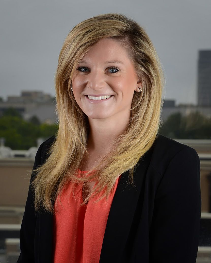 Denver Professional headshot of a person in a black blazer and coral top smiling against a cityscape background.
