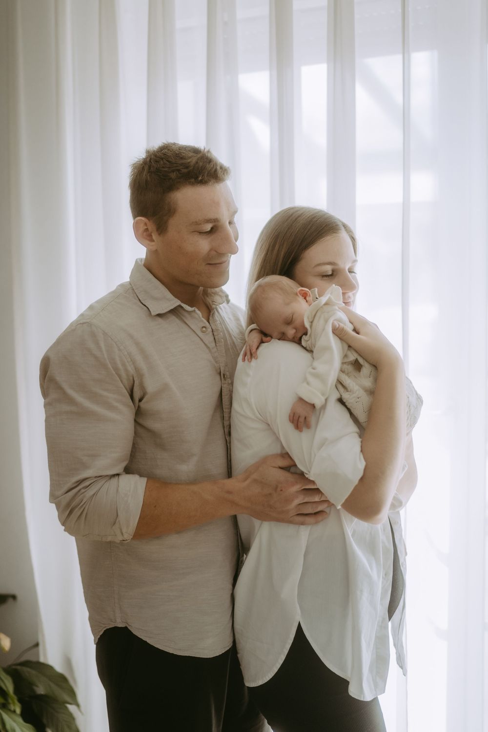 Mama und Papa stehen mit Baby vor dem Fenster