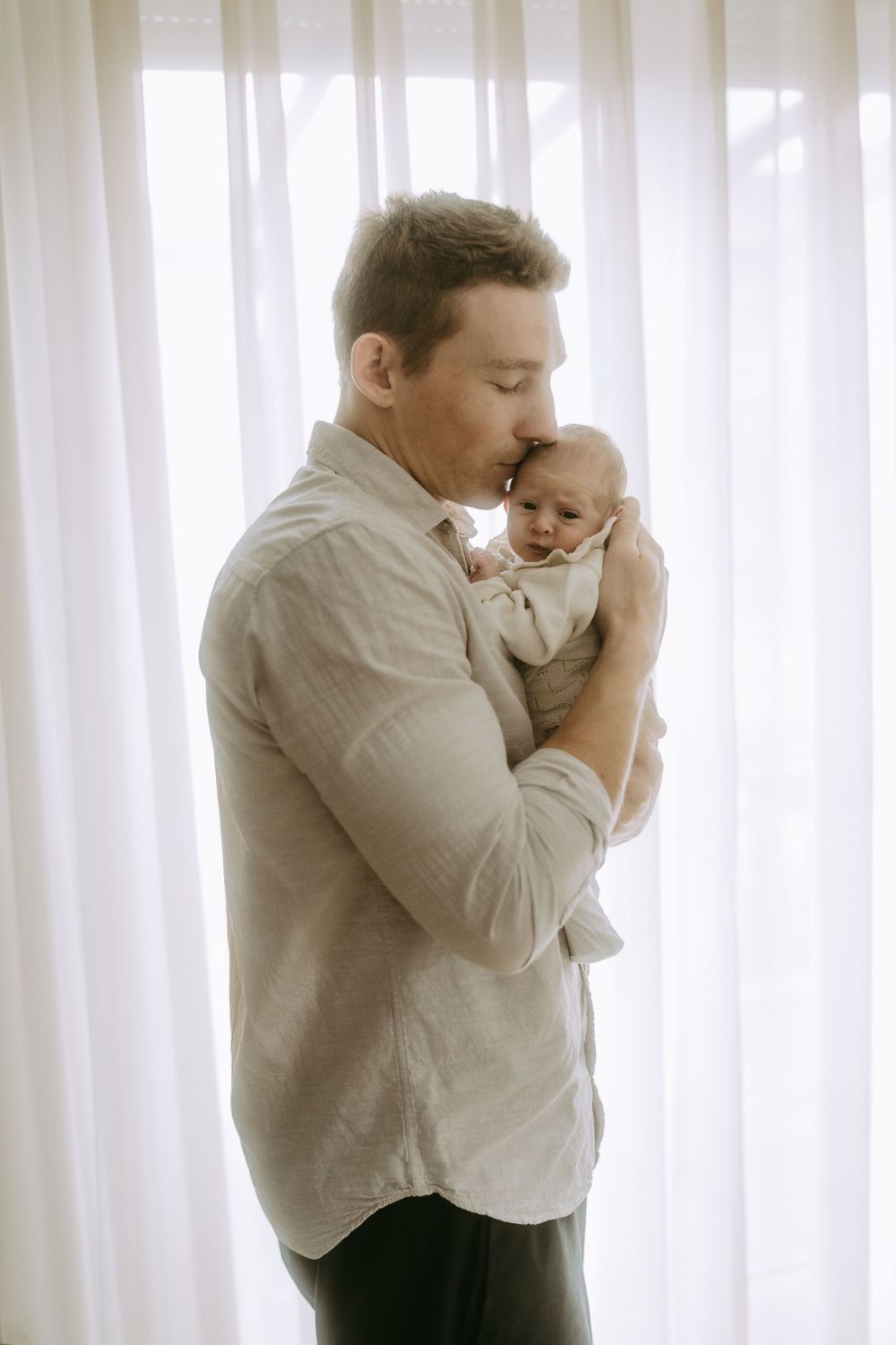 Papa küsst Baby vor dem Fenster auf Kopf