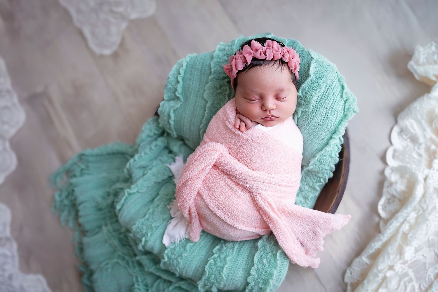 Child Photographer in Ponce baby lays wrapped in a pink blanket on a wooden bowl