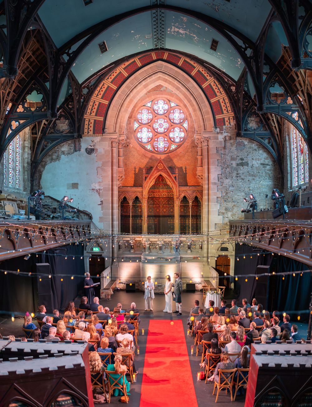 Gothic church interior with stained glass windows and red carpet setup for wedding ceremony.