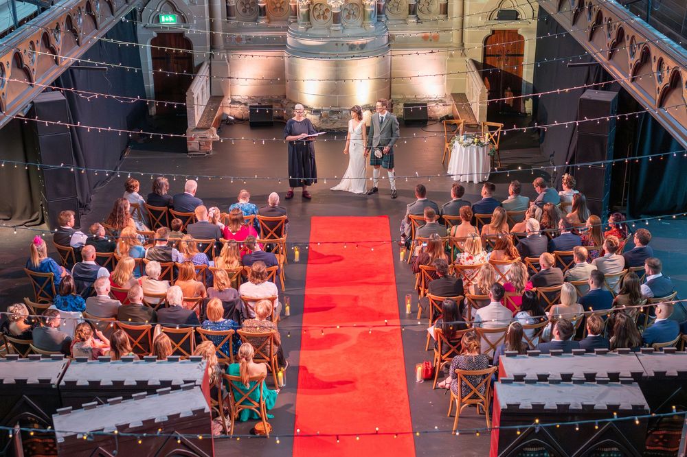 Wedding ceremony venue with wooden chairs arranged along a red carpet aisle in a historic church.