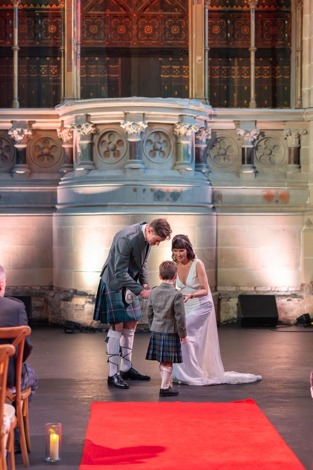 Wedding ceremony in progress on red carpet with historic church architecture in background.