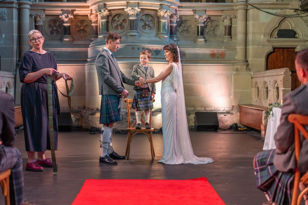 Wedding ceremony proceedings on red carpet in an elegantly lit historic venue.