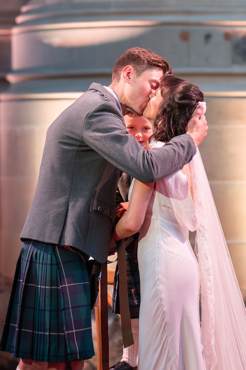 A romantic wedding kiss sequence between a couple where the groom wears a traditional Scottish kilt and grey jacket.
