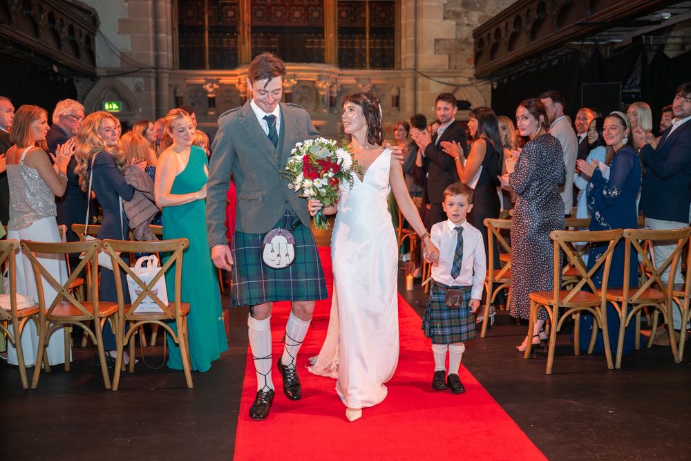 Large group wedding photo of guests and wedding party outside a stone church building.