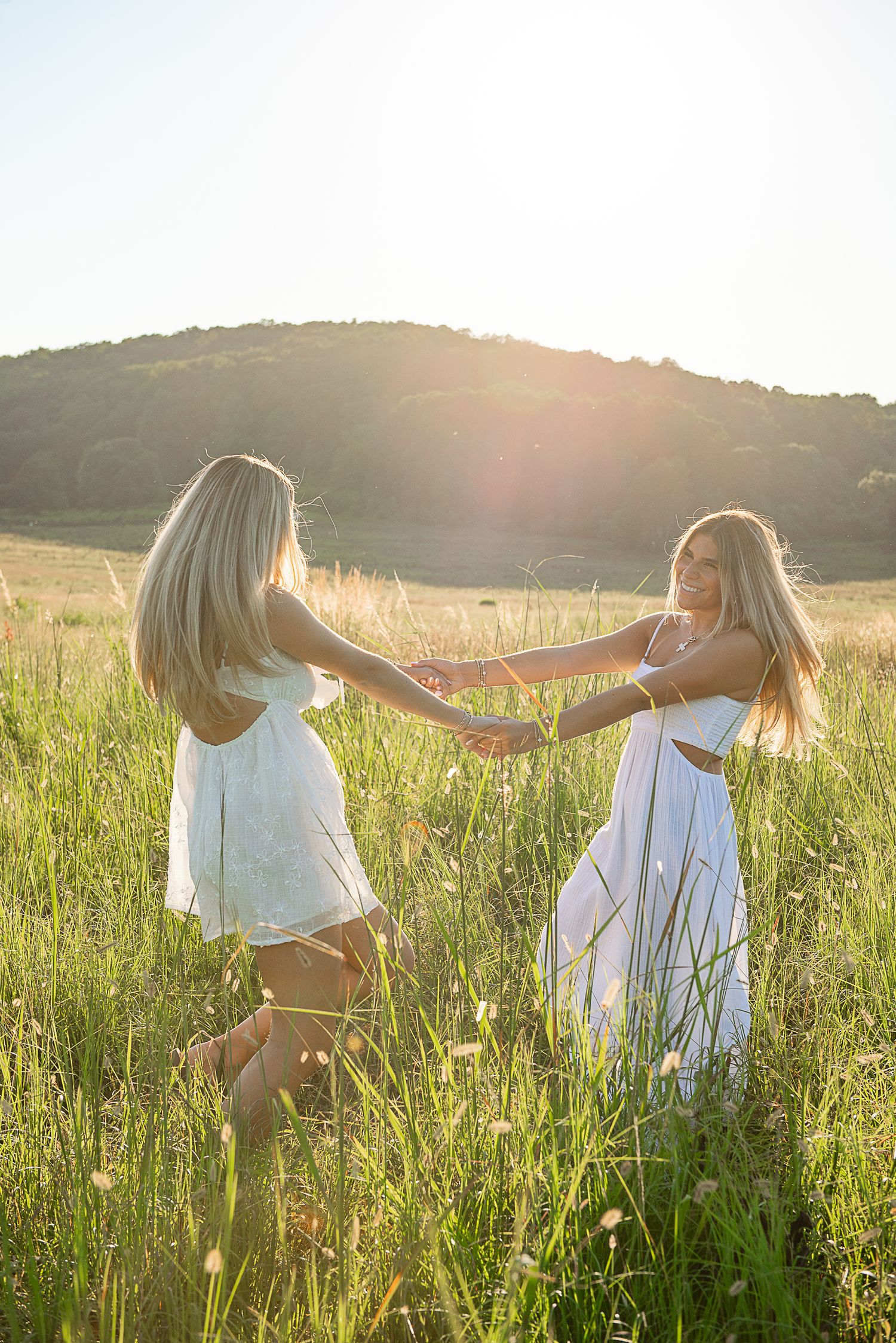 Two people in white outfits walk through a sunlit meadow of tall grass during golden hour.