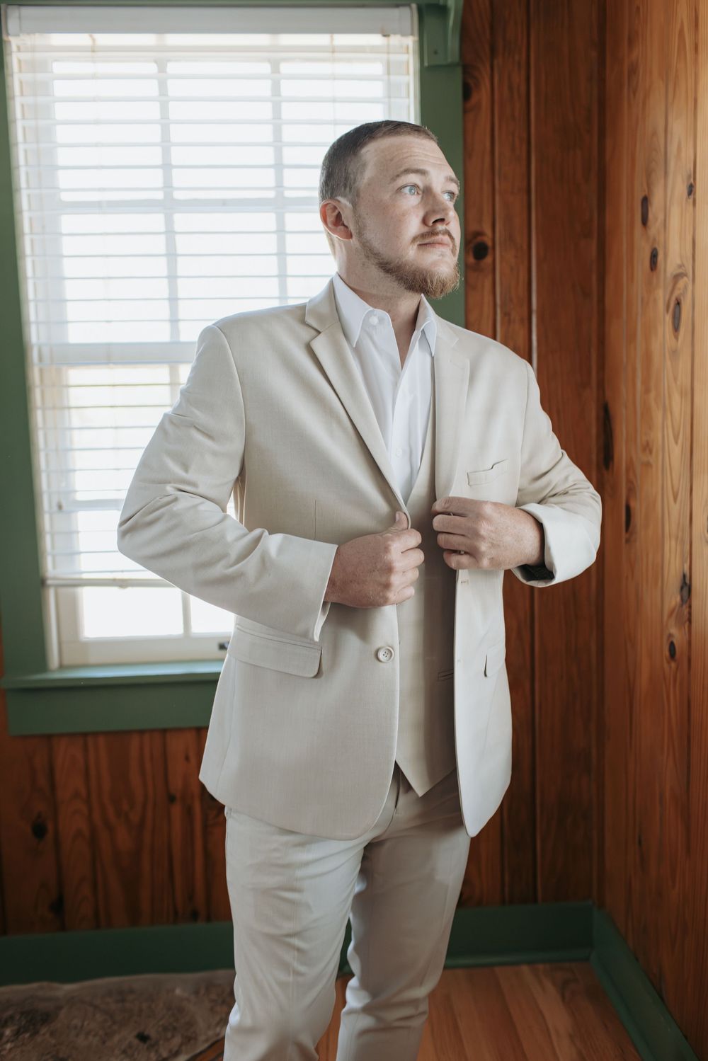Sequence of groom putting on light colored tie in rustic wooden room.