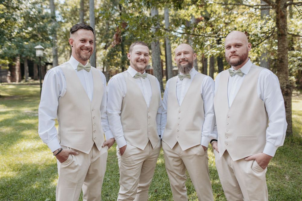 Groomsmen lined up outdoors wearing matching cream colored suits and brown shoes.