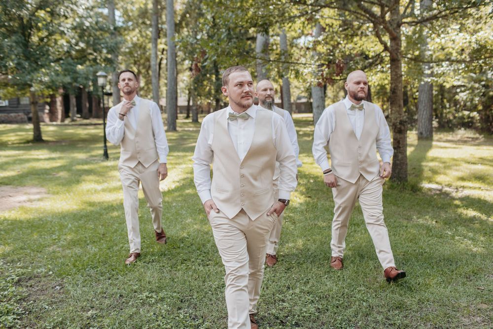 Wedding party in cream suits walking across a sunlit grassy area.