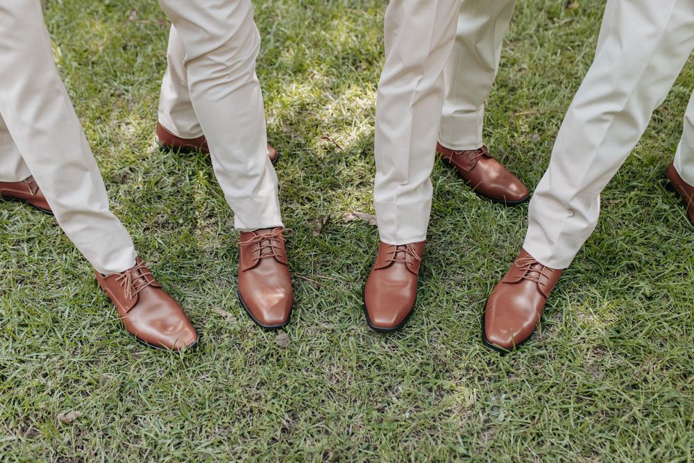 Row of brown leather dress shoes worn by groomsmen in cream colored pants.